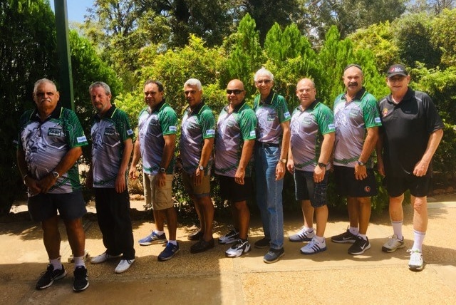 Nine men all in the same polo shirts face side on and pose for a photo.