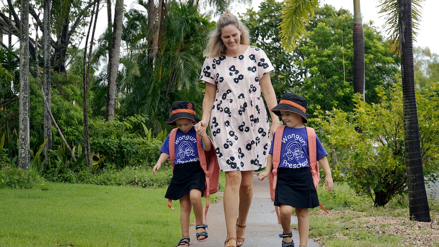 A woman and two primary-school aged girls walking along a path surrounded by greenery.