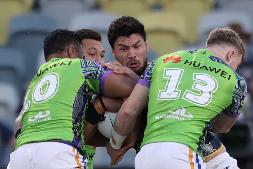 A North Queensland NRL player is tackled by three Canberra Raiders opponents.