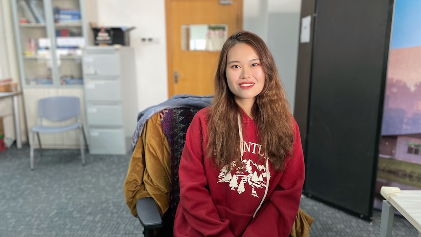 A Chinese girl dressed  in red sits on a black chair.