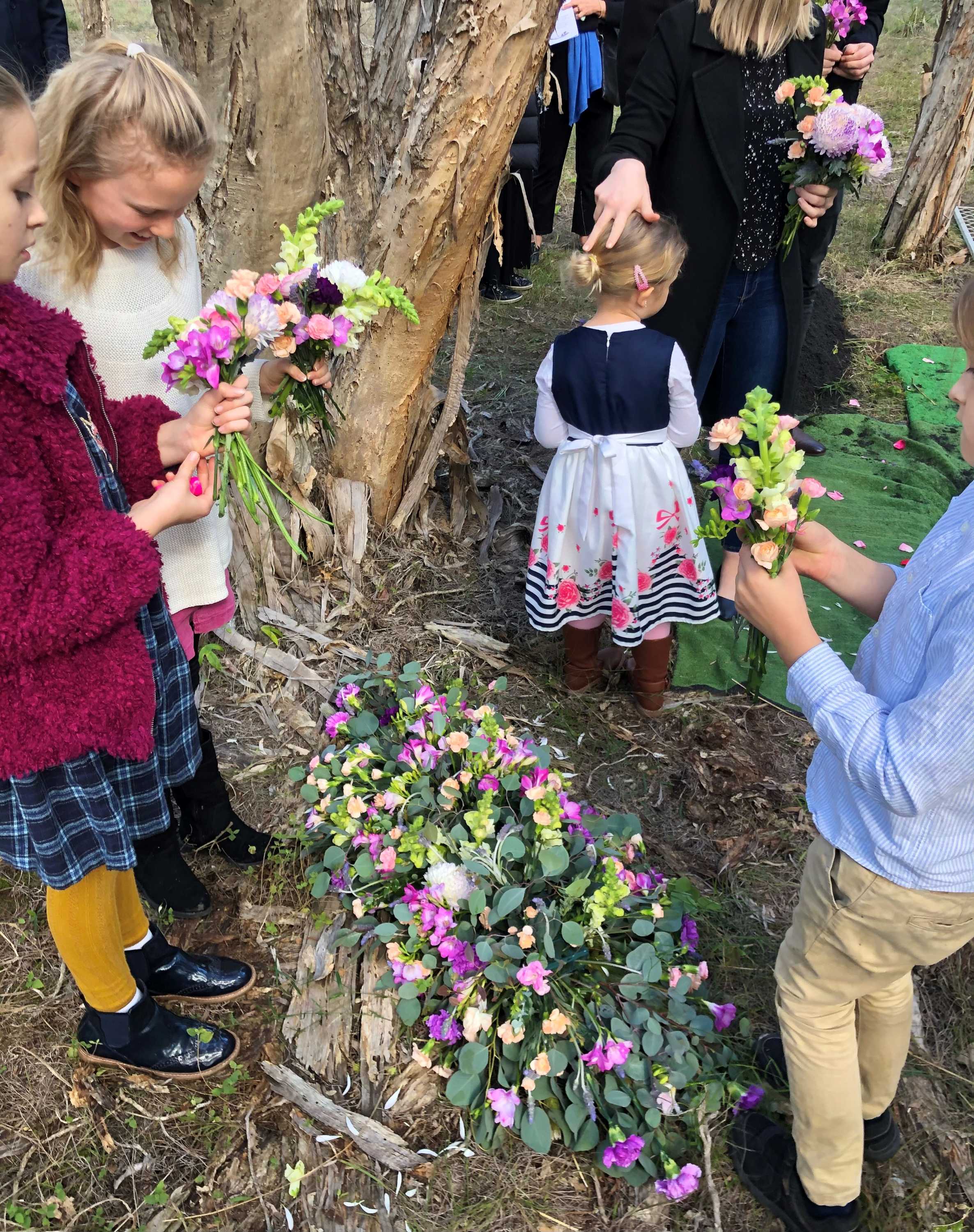 Some children collecting flowers near a tree for a natural burial.