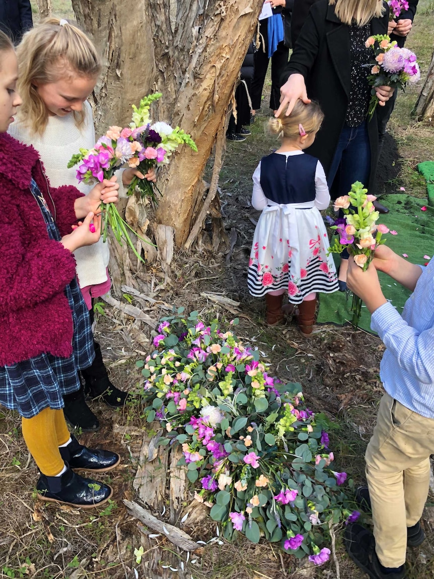 Certains enfants ramassent des fleurs près d'un arbre pour un enterrement naturel.