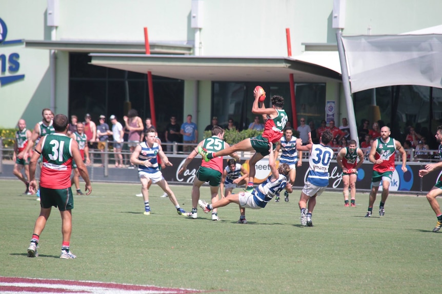 An AFL player in a red and green jersey takes a high-flying mark over an opponent.