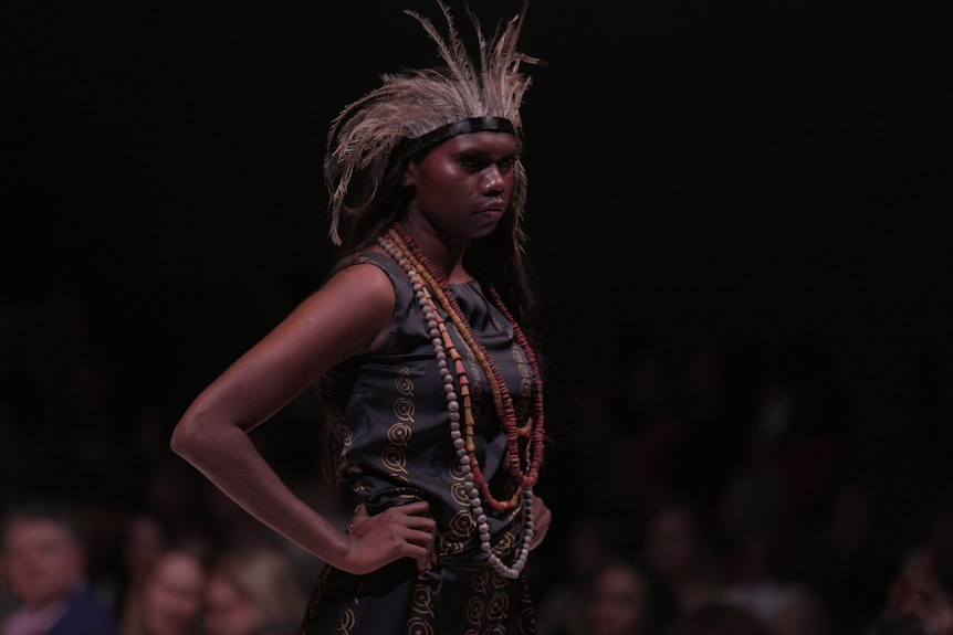 a female model wears a black dress, head piece and beads