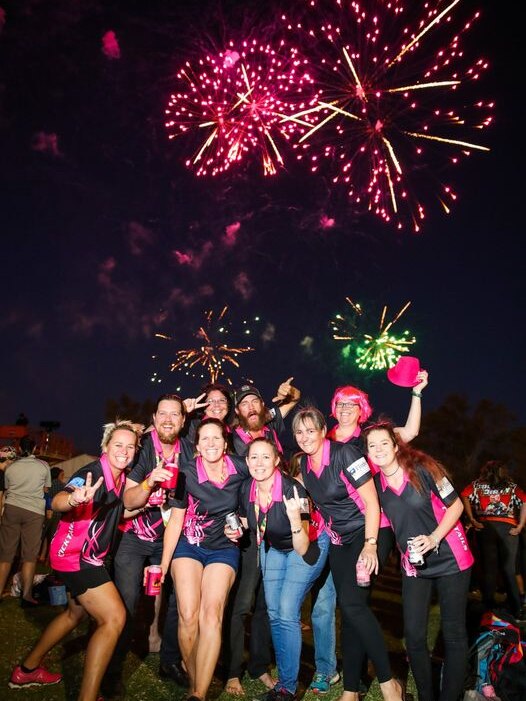 Un groupe d'athlètes portant du noir et du rose la nuit avec des feux d'artifice rose foncé en arrière-plan.