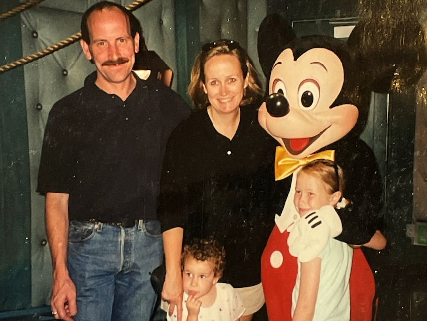 A man, a woman, and two small girls pose with Mickey Mouse 