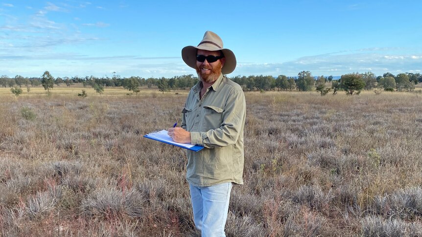 A man stands in a brown paddock.
