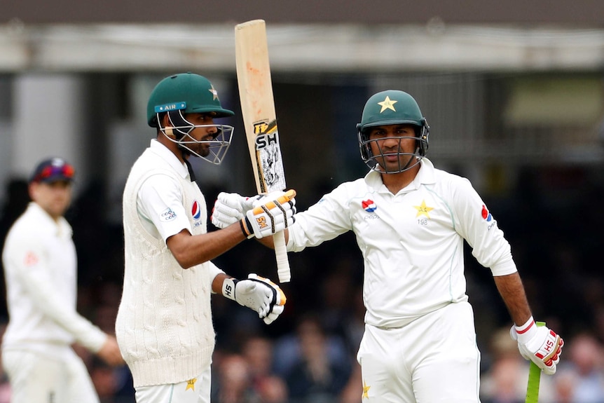 A cricketer raises his bat for reaching 50, as his teammate pats him with his glove in celebration.