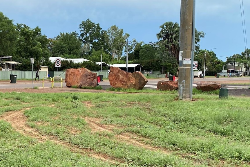 large rocks at an intersection in a town near tyre marks in the grass