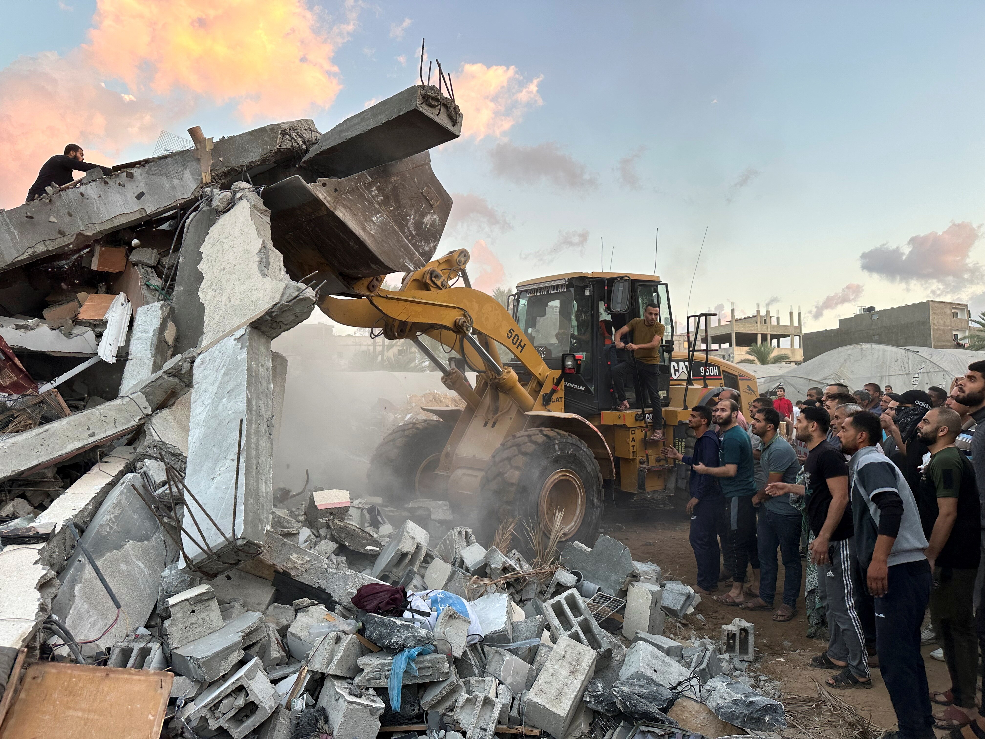A truck lifts the debris of a building as people watch on 