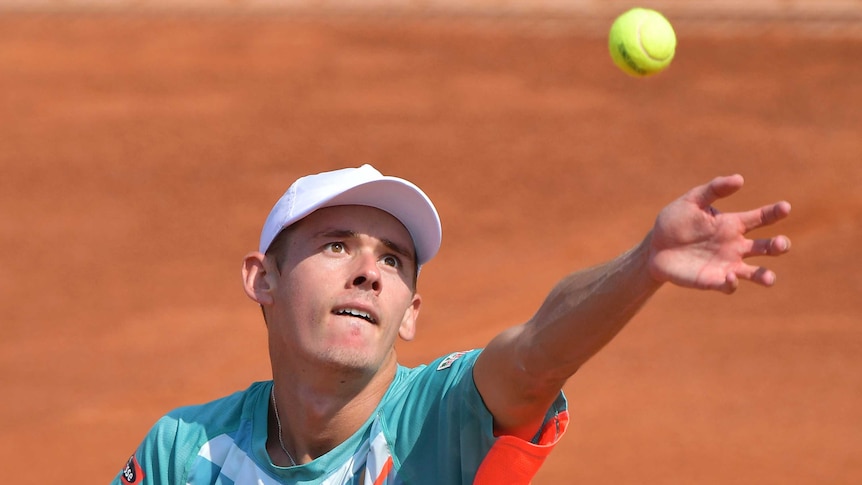 Alex de Minaur throws a ball in the air, ready to hit it with a tennis racket in a serving motion at the Italian Open.