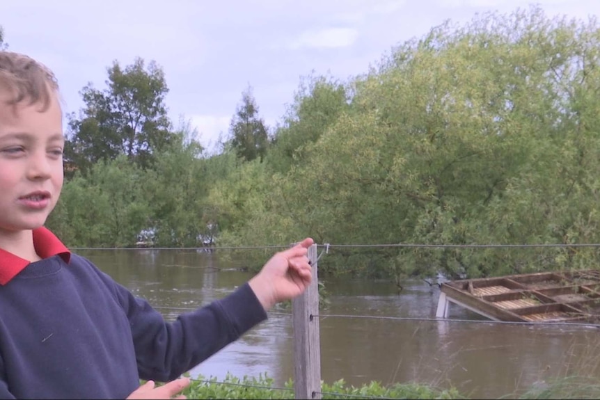 A young boy stands in front of floodwaters