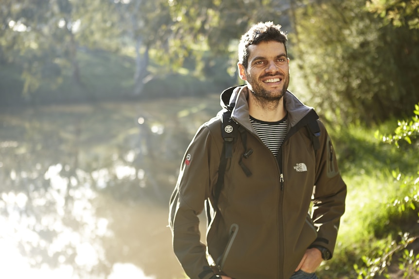 A man standing by a river, with a backpack on.