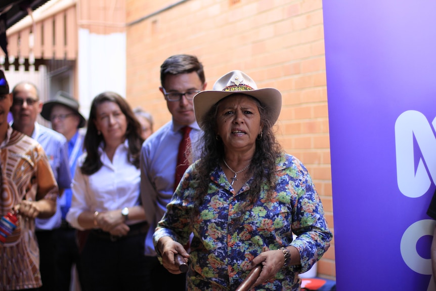 A woman talking to the camera, holding clapping sticks. 