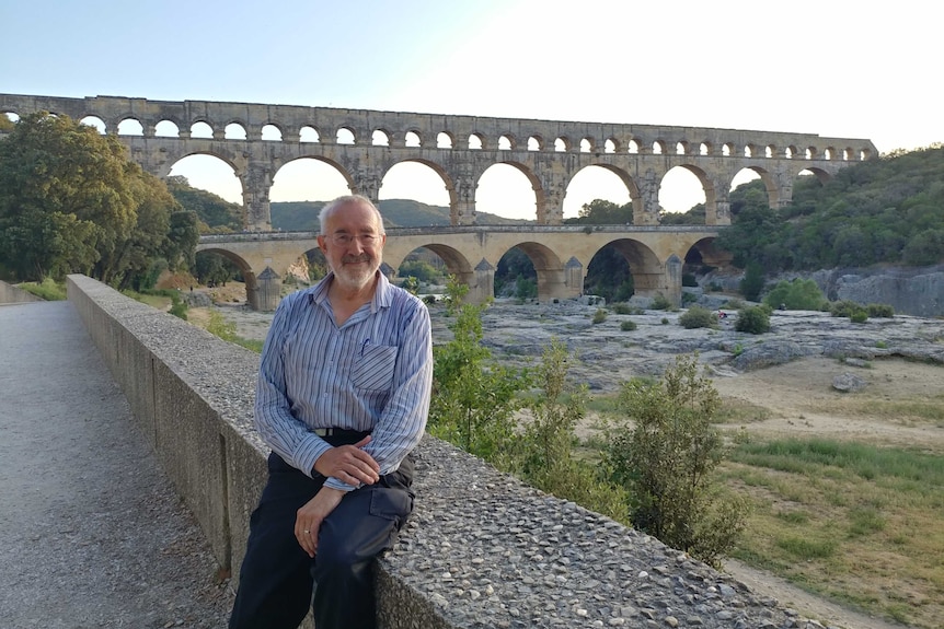 Robin Wiley stands in front of an ancient three-tiered Roman aqueduct spanning the Gardon River in France.