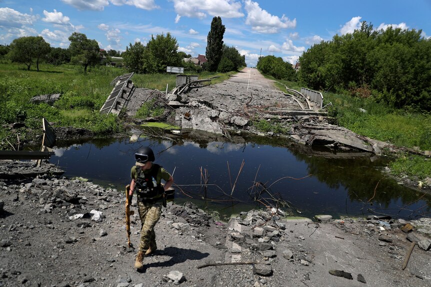 Soldier walks by damaged road filled with water.
