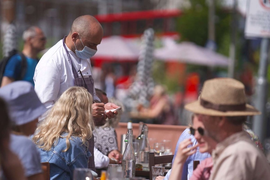 A man wearing a mask taking customers meal orders.