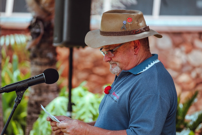 A man in a hat standing near a microphone.