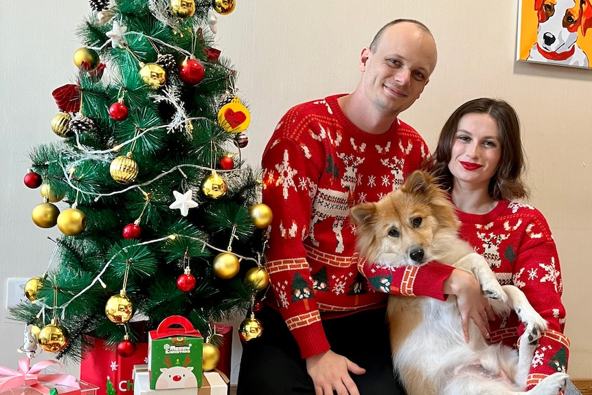 A couple sitting next to a christmas tree with their dog
