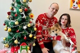 A couple sitting next to a christmas tree with their dog