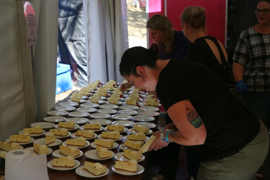 A woman adds cream to a table filled with plates of cheesecake.