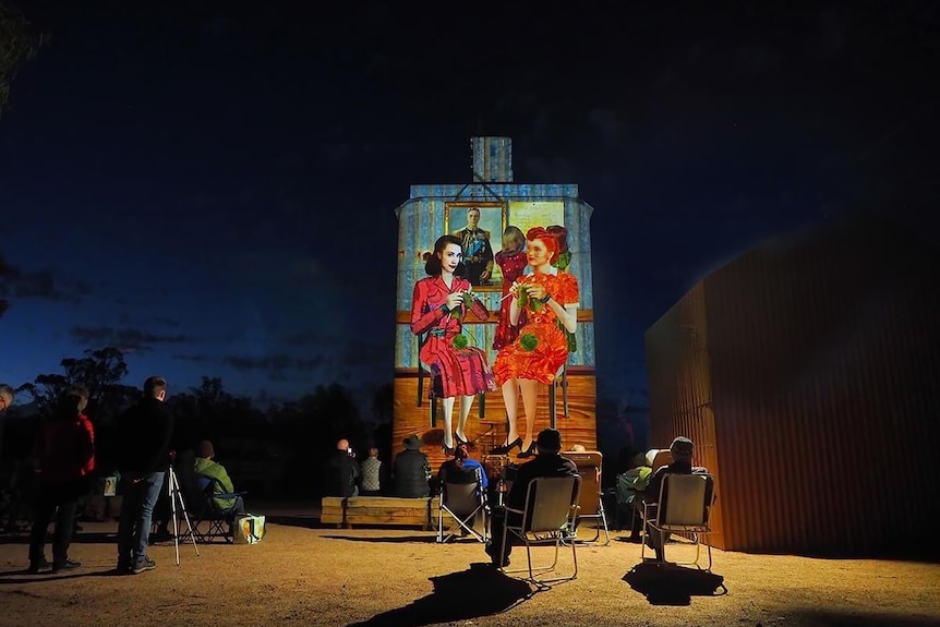 A silo with two women projected onto it as light art.