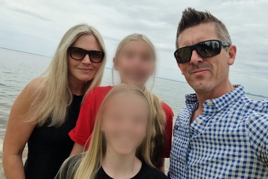 A family on the beach, two kids with faces blurred. 