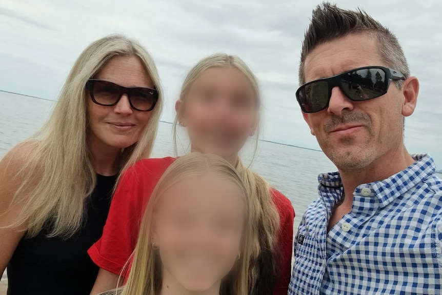 A family on the beach, two kids with faces blurred. 