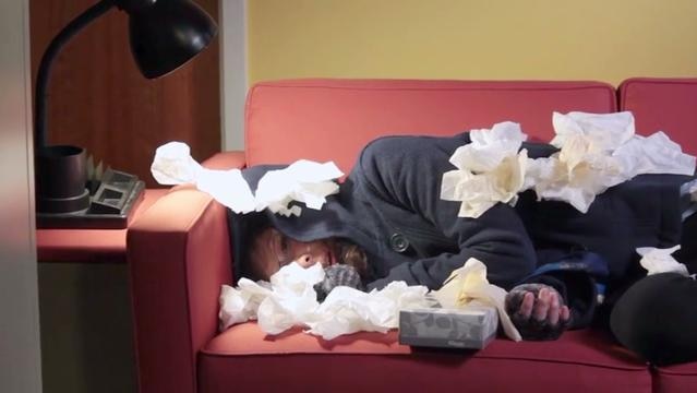 Person lays on couch under pile of used tissues