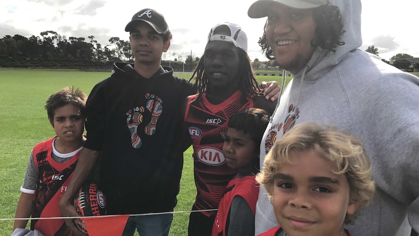 Kids stand around Essendon player Anthony McDonald-Tipungwuti.