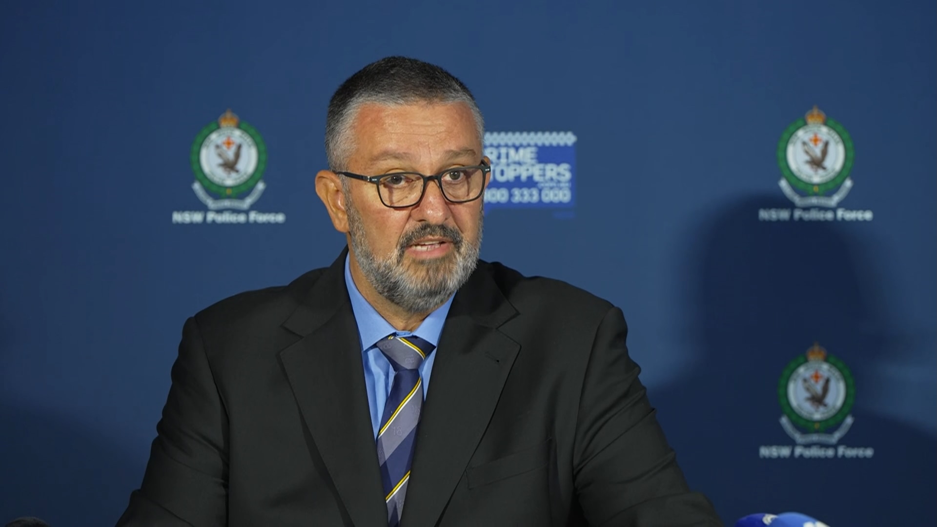 Superintendent Doueihi talking at a press conference, wearing glasses and a suit.