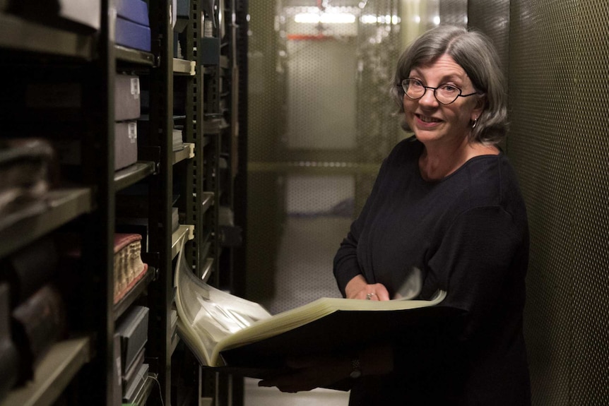 Curator of the State Library of NSW Maggie Patton looks through a photo album amongst the archive stacks