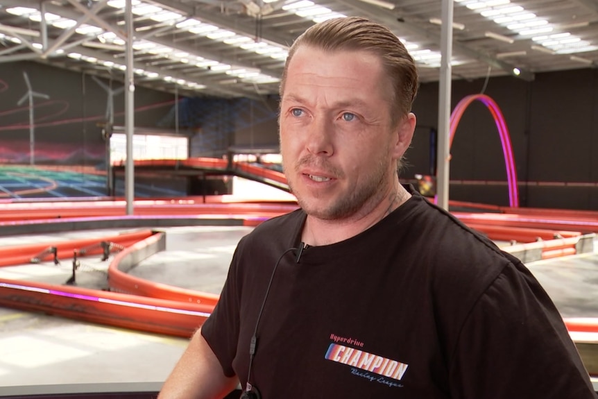 Man in black t-shirt stands in front of go-karting track 