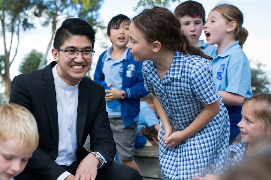 Father Justel crouches down, surrounded by kids.