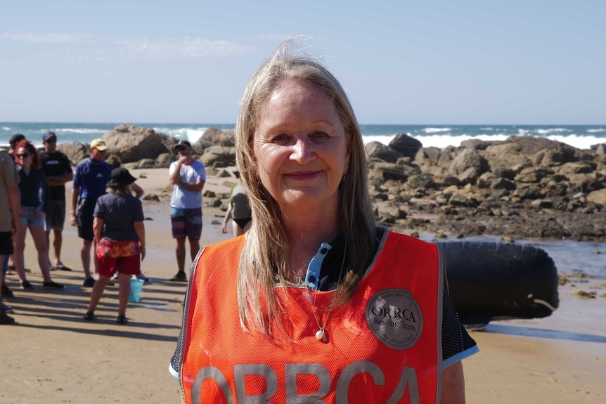 A head and shoulders portrait of a woman at the beach. She has short blonde hair, and she's wearing a high vis vest