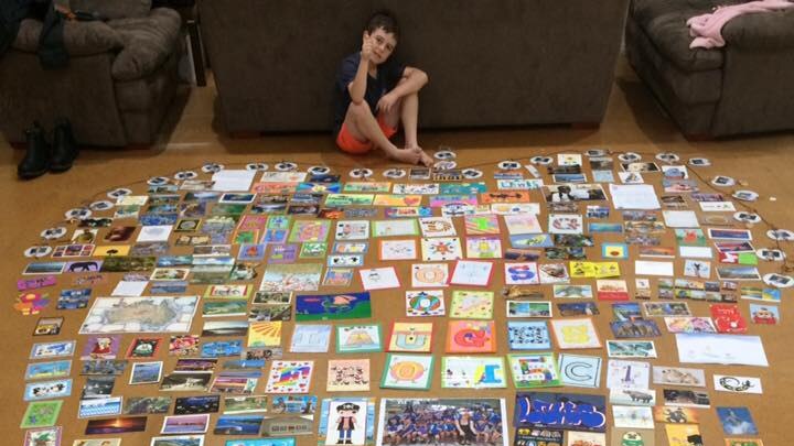 Boy sitting in front of hundreds of postcards and drawings in the shape of a love heart.