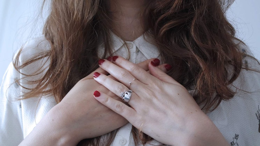 A woman holds her hands over her heart.