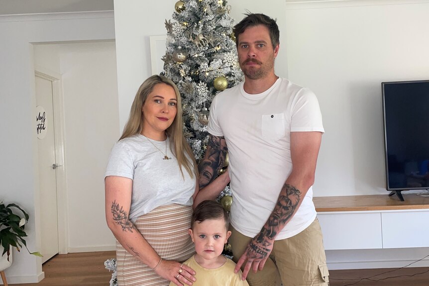 Justin y su esposa e hijo se paran frente a un árbol de navidad plateado con adornos blancos y dorados 