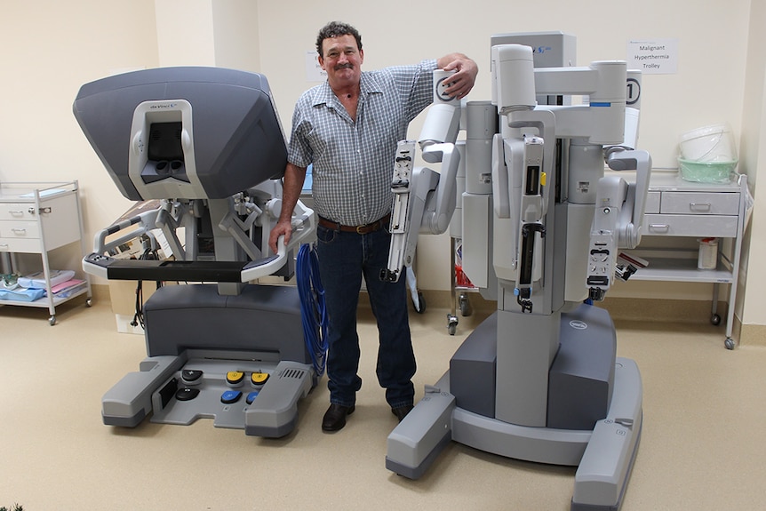 Patient Trevor Bennett gives the DaVinci robot a 'hug' at St Andrews Hospital Toowoomba