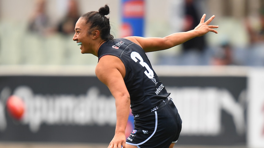 A Carlton AFLw player runs with her arms apart as she celebrates kicking a goal.