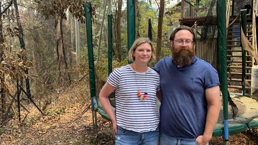 Kirsty and Rob Mitchell stand in their backyard near a burnt trampoline and charred trees