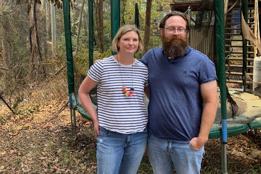 Kirsty and Rob Mitchell stand in their backyard near a burnt trampoline and charred trees