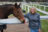 Townsville resident Heather White leans on a white fence with a horse nuzzling her arm.
