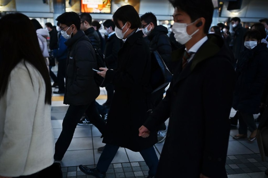Mask-clad commuters on their way to work during morning rush hour in Tokyo