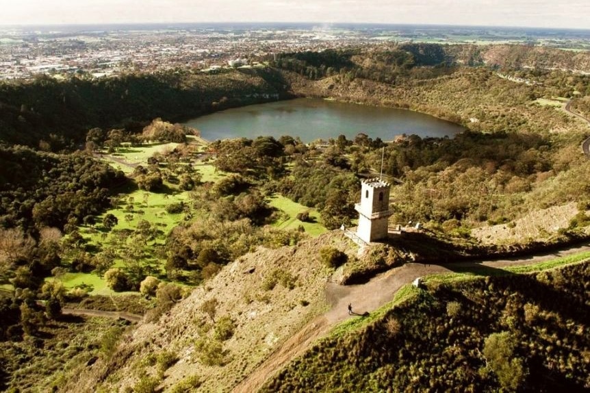 A tower topped with a turret sits on a hill overlooking a green valley with a large lake.