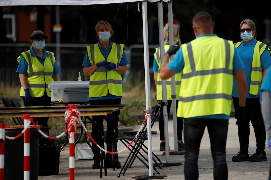 Medical staff wearing yellow vests and white face masks wait for people to arrive for COVID-19 testing.