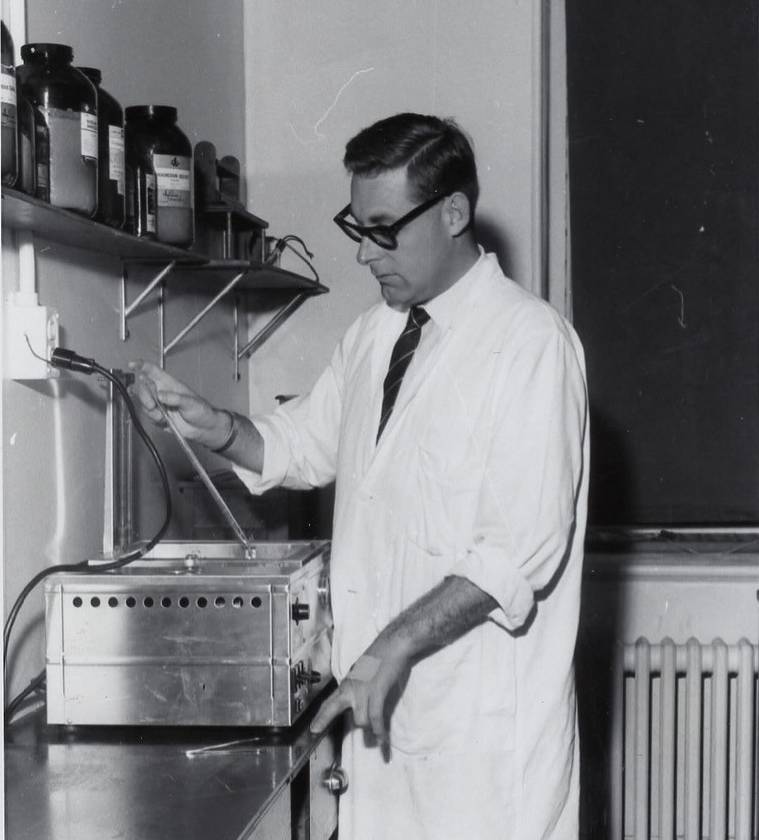 A middle-aged man in a white coat testing substances in a laboratory. 