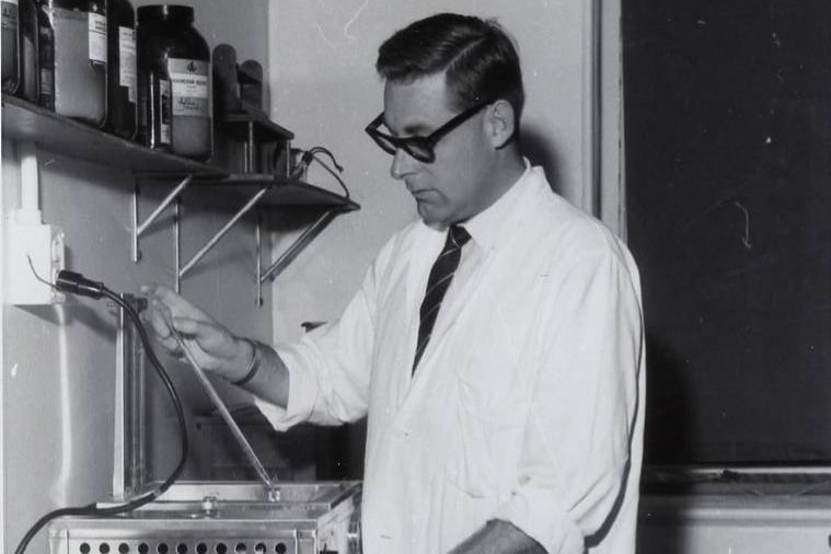 A middle-aged man in a white coat testing substances in a laboratory. 