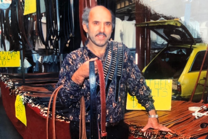 A man holds leather belts at a market stall in the 1990s