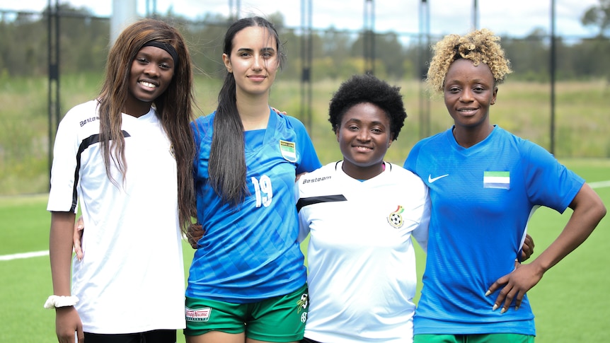 Four women stand, arms around each other, smiling at the camera.